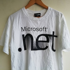 Peut inclure: T-shirt blanc avec un logo Microsoft .NET noir imprimé sur le devant. Le logo est en police épaisse sans empattement.