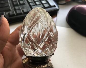 May include: A clear glass egg with a diamond pattern sits on a silver stand with ornate details.
