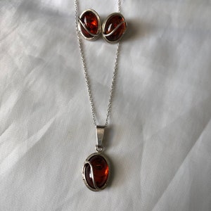May include: A silver necklace and earrings set with oval amber stones. The stones are set in a silver frame with a delicate swirl design.