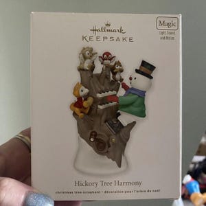 May include: A Hallmark Keepsake Christmas tree ornament titled "Hickory Tree Harmony." The ornament features a snowman playing a piano with several woodland creatures. The box reads "Magic Light, Sound, and Motion."