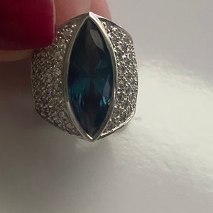 May include: A silver ring with a large, dark blue marquise-shaped gemstone surrounded by smaller, clear gemstones.