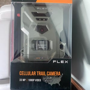 Könnte beinhalten: Eine zellulare Wildkamera in einer Box. Die Kamera ist grau mit dem Text "FLEX" und "SPYPOINT". Auf der Box steht "CELLULAR TRAIL CAMERA" und "33 MP | 1080P VIDEO". Die Kamera hat ein rotes Objektiv und einen Aufkleber mit der Aufschrift "Remove tape before use".