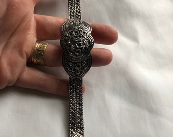 May include: A silver bracelet with a chain link design and three round, ornate, silver medallions. The medallions have a floral pattern.