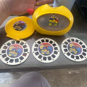 May include: A yellow plastic projector with a clear viewing window and a picture of The Wiggles on the front. Three round, white plastic reels with pictures of The Wiggles are also included.
