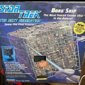 May include: A Star Trek: The Next Generation Borg Ship toy box. The box features the Borg cube ship design, with text that reads "The Most Feared Enemy Ship in the Galaxy!" and "Actual Sounds from the Star Trek: The Next Generation T.V. Show!"