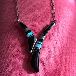 Puede incluir: Un collar de cadena de plata con un colgante negro y blanco con una incrustación de ópalo azul y blanco.