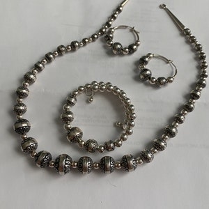 May include: A silver necklace, bracelet, and earrings set with decorative beads. The beads are round and have a textured surface.