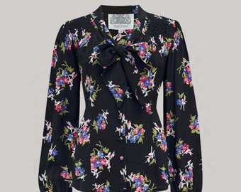 May include: A black long-sleeved blouse with a floral print and a bow tie. The blouse has a fitted bodice and a slightly flared skirt. The fabric is a lightweight silk.