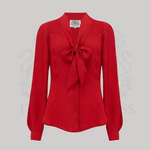 Puede incluir: Una blusa roja de manga larga con lazo y cierre de botones.