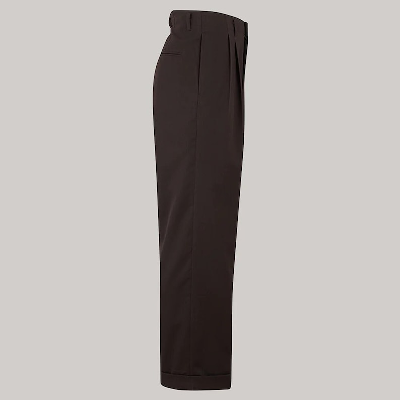 Puede incluir: Pantalones plisados marr&oacute;n oscuro con dobladillo vuelto. Los pantalones tienen un dise&ntilde;o cl&aacute;sico y a medida, con cintura alta y corte relajado. La tela parece ser de color liso y suave, adecuada para diversas ocasiones.