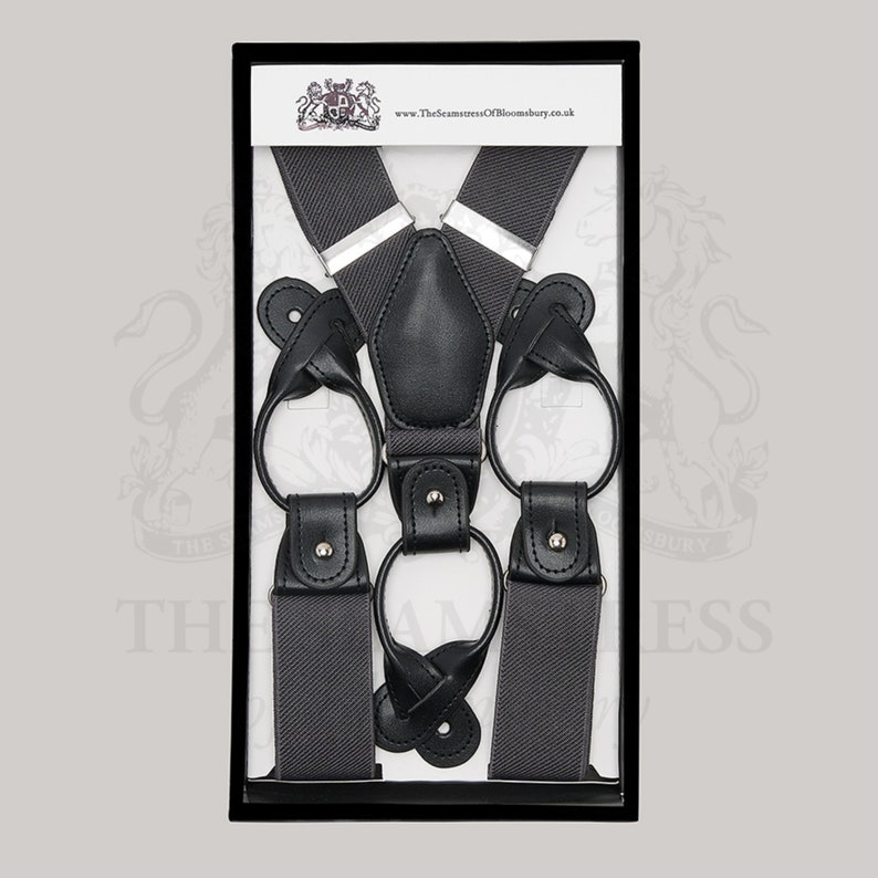Puede incluir: Tirantes gris oscuro con detalles de cuero negro, presentados en una caja negra. Los tirantes presentan un dise&ntilde;o cl&aacute;sico con presillas de cuero y ajustadores met&aacute;licos. El producto se muestra sobre un fondo blanco.
