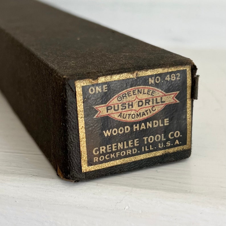 Puede incluir: Un taladro de empuje Greenlee vintage en su caja original. La caja es de color marr&oacute;n oscuro con una etiqueta dorada que dice "Greenlee Push Drill Automatic Wood Handle". La etiqueta tambi&eacute;n incluye el texto "Greenlee Tool Co. Rockford, Ill. U.S.A."