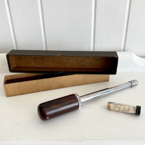 Puede incluir: Un taladro Yankee vintage con un mango de madera oscura y un eje de metal plateado, junto a su caja de cart&oacute;n original. Tambi&eacute;n hay un peque&ntilde;o vial de vidrio con puntas de taladro. El taladro es una herramienta manual.
