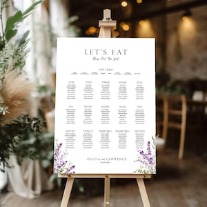 May include: A white wedding seating chart on an easel, featuring the text "LET'S EAT" and guest names. Lavender and white floral accents frame the bottom corners. The names "Olivia and Lawrence" and a date are also included.