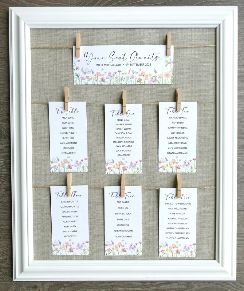 Lilac, Pink, Peach and Yellow Wildflower Print Wedding Seating Plan Cards shown pegged on string in a white frame and grey linen background