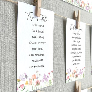 Lilac, Pink, Peach and Yellow Wildflower Print Wedding Seating Plan Cards shown pegged on string in a white frame and grey linen background