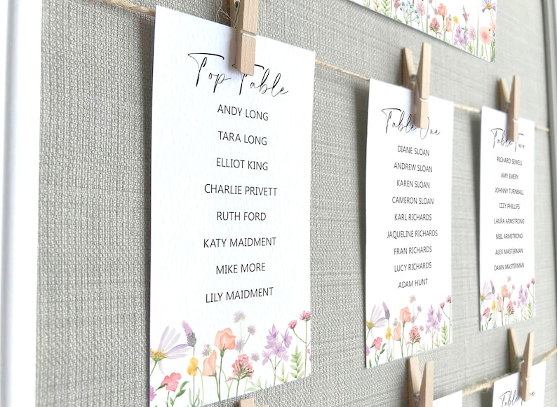 Lilac, Pink, Peach and Yellow Wildflower Print Wedding Seating Plan Cards shown pegged on string in a white frame and grey linen background