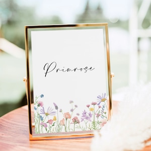 White wedding table number card  featuring a pink, lilac, yellow and peach wildflower design on a white background. Shown in a gold coloured frame on a wooden table