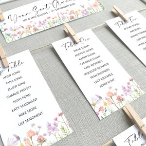 Lilac, Pink, Peach and Yellow Wildflower Print Wedding Seating Plan Cards shown pegged on string in a white frame and grey linen background