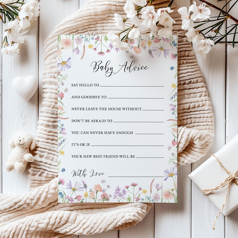 Baby Advice Baby shower game card featuring a pink, yellow, Lilac and peach wildflower design on a white background. Shown flat on a beige cloth surrounded by white flowers, a white heart and a small teddy bear