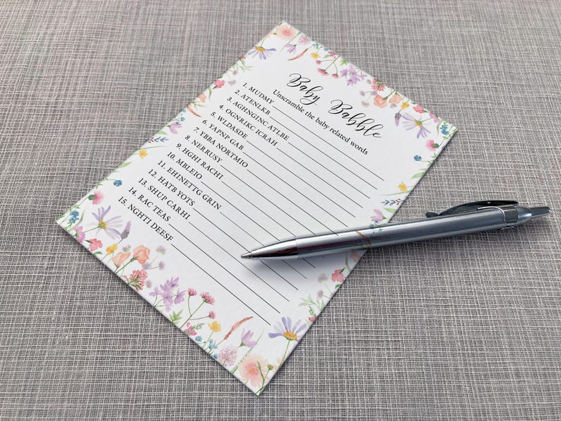 Baby Babble Baby shower game card featuring a pink, yellow, Lilac and peach wildflower design on a white background. Shown alongside a pen