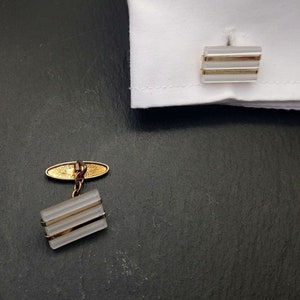 May include: A pair of cufflinks with a gold-tone finish and clear glass inserts. The cufflinks have a simple, elegant design and are perfect for adding a touch of sophistication to any outfit.