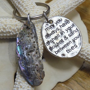 May include: A silver keychain with a seashell charm and a round tag that reads "May you always have a shell in your pocket & sand between your toes".