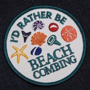 Peut inclure: Patch brodé blanc avec des points de couture turquoise. Le patch présente le texte "I'd Rather Be Beach Combing" avec une variété d'illustrations sur le thème de la mer, notamment une étoile de mer, une coquille et une coquille.