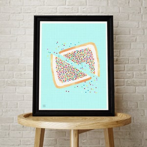 May include: A framed print of a colorful illustration of a broken Australian lamington, a traditional Australian dessert, on a blue background with a grid pattern.