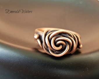 May include: A copper ring with a spiral design. The ring is made of twisted wire and has a dark patina.