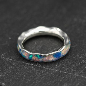May include: A silver ring with a textured band and a blue, pink and green opal inlay.