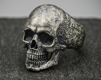May include: A silver skull ring with a detailed design. The skull has a textured surface and a defined jawline.
