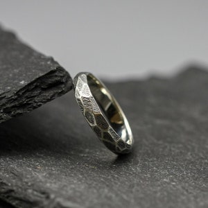 Könnte beinhalten: Ein silberner Ring mit einer strukturierten, gehämmerten Oberfläche. Der Ring liegt auf einem Stapel schwarzer Schieferplatten.