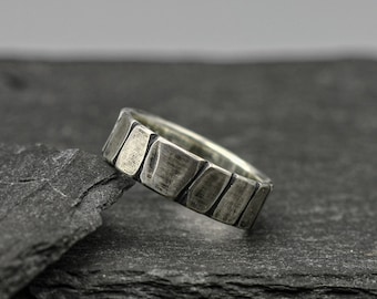 May include: A silver ring with a textured, segmented design. The ring is made of multiple small, rectangular pieces that are joined together to create a unique and modern look.