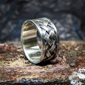 May include: A silver ring with a braided design. The ring is made of metal and has a polished finish.