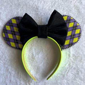 May include: Black bow headband with yellow and purple plaid ears. The headband is neon green.
