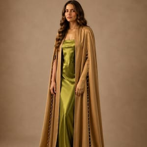 May include: A floor-length olive green satin slip dress paired with a long, tan-colored cape. The cape features a straight, open front and is detailed with a vertical row of small, round, metallic buttons along the outer edges of the arm openings.
