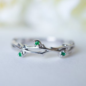 May include: A silver ring featuring a delicate branch design with three small green gemstones.