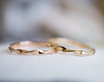 May include: Two delicate, twisted metal rings. One ring is rose gold, the other is gold. The rings are thin and have a wavy, textured design. The rings are likely for a wedding or engagement.