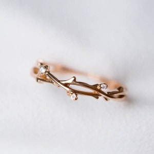 May include: A delicate gold ring featuring a twig design with small clear stones.
