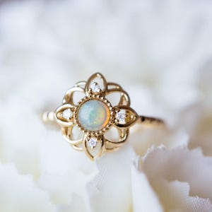 May include: A gold ring featuring a delicate floral design and a round opal gemstone in the centre. The ring is set with small diamonds around the opal.