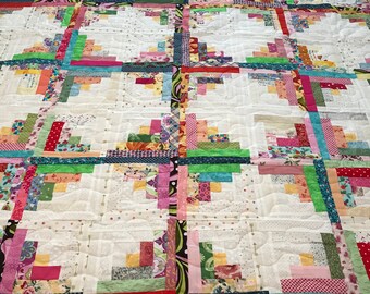May include: A colorful quilt with a log cabin pattern. The quilt is made with a variety of fabrics in shades of pink, green, yellow, red, and blue. The quilt is quilted with a simple stitch pattern.