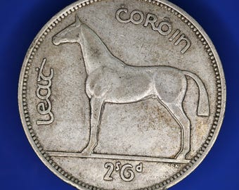May include: A silver coin featuring a horse with the text "Leat" and "Coroin" around the edge. The coin also has the number "2/6d" at the bottom. The coin is set against a blue background.