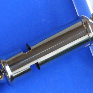 May include: A silver whistle with a round ring on the top. The whistle has a smooth, shiny surface.