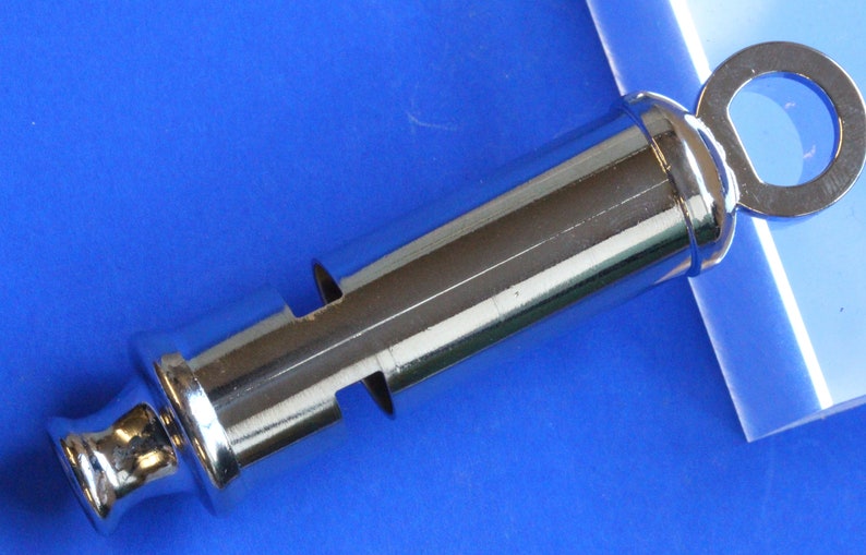 May include: A silver whistle with a round ring on the top. The whistle has a smooth, shiny surface.