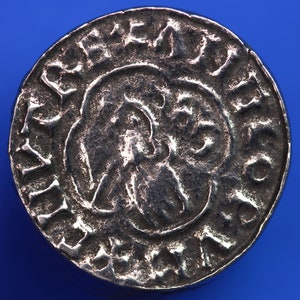 May include: A silver coin with a raised design of a bird with its wings spread. The coin has a circular inscription around the edge.