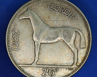 May include: A silver coin featuring a horse in profile, with the word "COROIN" arched above. The coin also has the text "LEAC" and "2'6d" along the edges. The coin has a detailed, textured surface.
