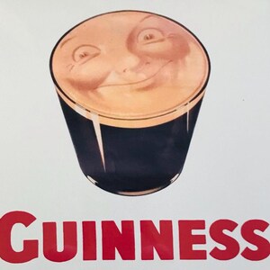 Może przedstawiać: Pintę piwa Guinness z uśmiechniętą twarzą na kremowej pianie. Szklanka jest ciemna, a słowo "GUINNESS" jest wydrukowane na czerwono na dole.