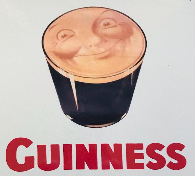 Może przedstawiać: Pintę piwa Guinness z uśmiechniętą twarzą na kremowej pianie. Szklanka jest ciemna, a słowo "GUINNESS" jest wydrukowane na czerwono na dole.