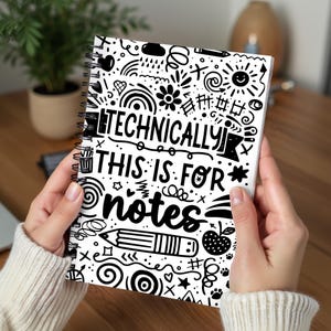 May include: A spiral-bound notebook with a white cover featuring a black doodle design. The cover includes the text "TECHNICALLY THIS IS FOR notes" in a playful font, along with various illustrations like a pencil, apple, and sun.